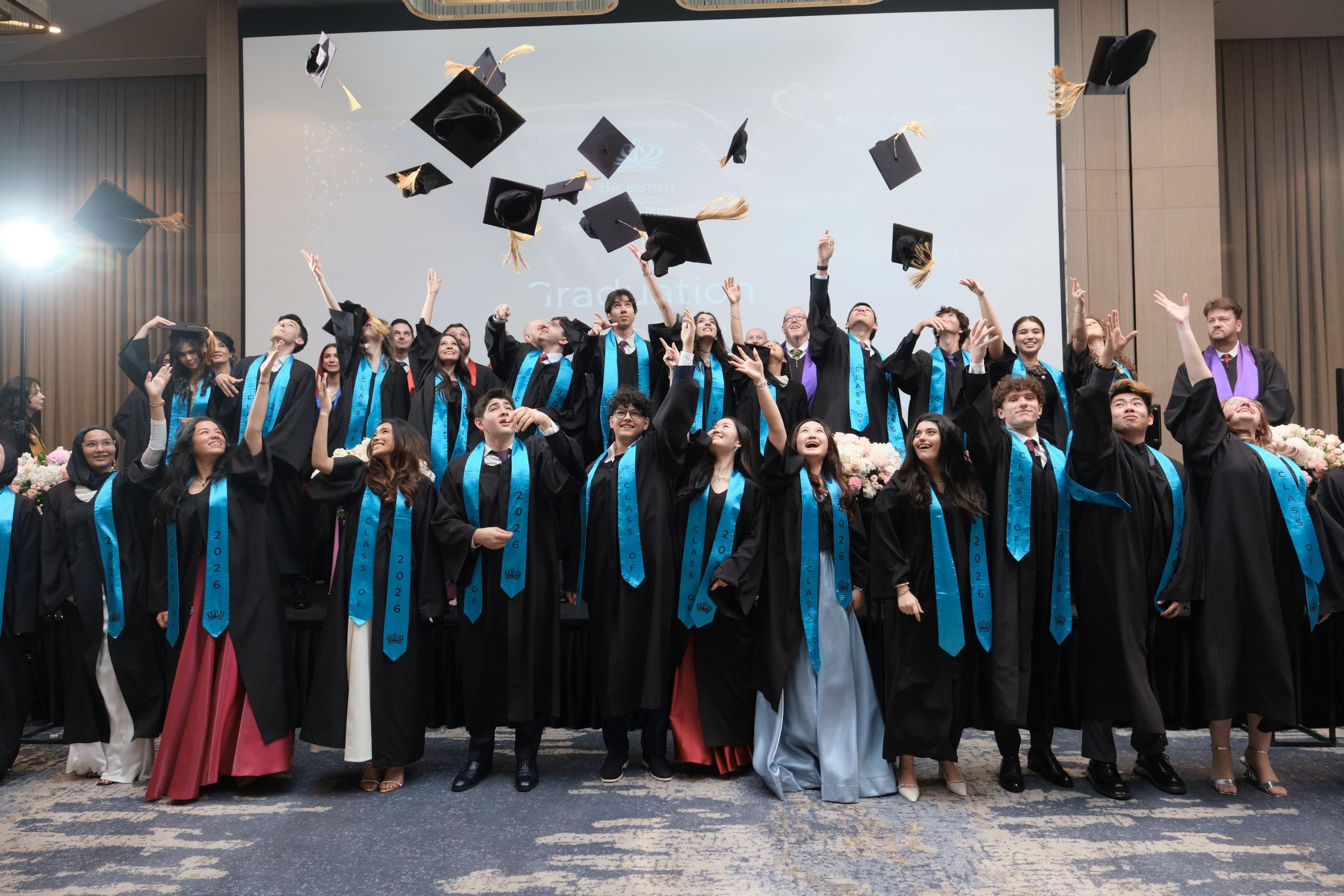 Students from The British School of Tashkent celebrating at Graduation by throwing their caps in the air
