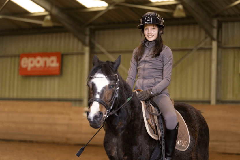 Young student riding a horse during an equestrian activity, gaining confidence through hands-on learning.