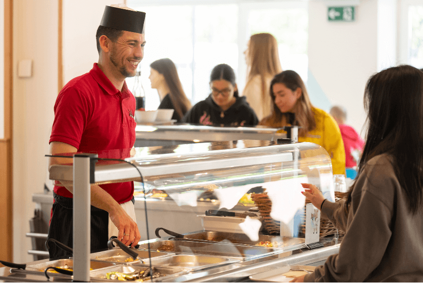 Friendly dining staff serving boarding students at lunch, highlighting warm, personal care and healthy meals.