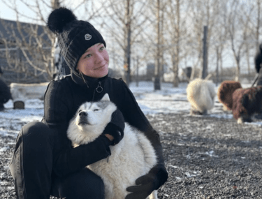 Boarding student cuddling a husky during a snowy outdoor excursion, building confidence and connection through adventure.