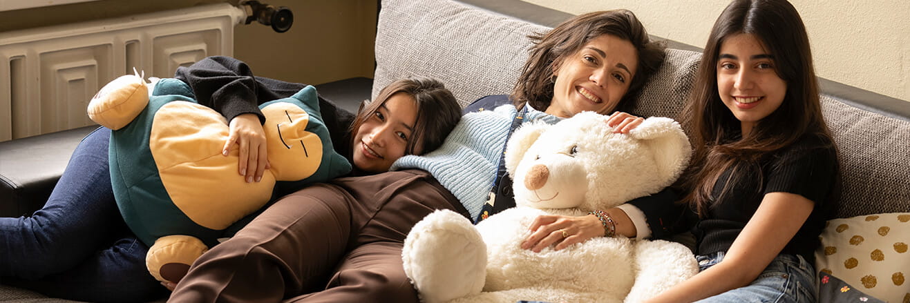 Two boarding students and a House Parent relaxing with stuffed animals on a sofa, sharing a warm and caring moment at Collège du Léman.