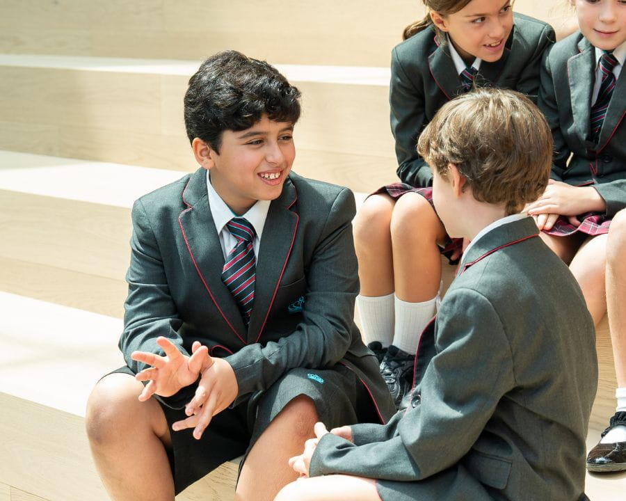 Primary school students in NAS Dubai school uniform sitting together and socialising in the school atrium.
