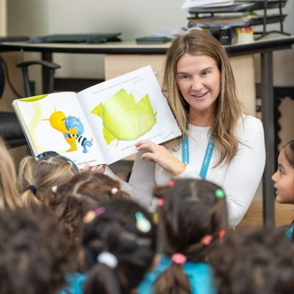 Primary school teacher reading book to young students