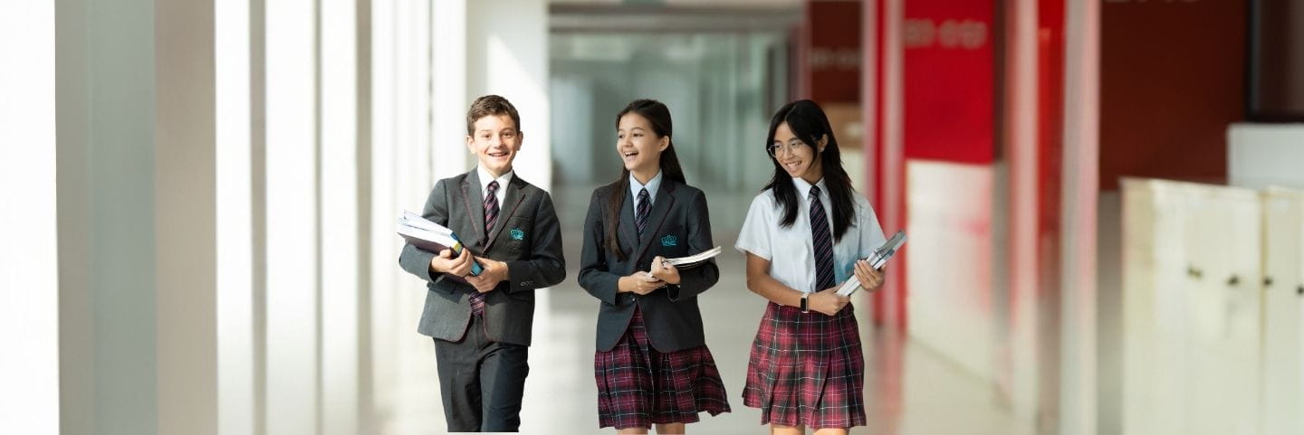 A group of students in school uniforms walk together through a bright, modern corridor while carrying books and notebooks.