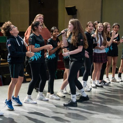 Secondary students singing and performing on stage 