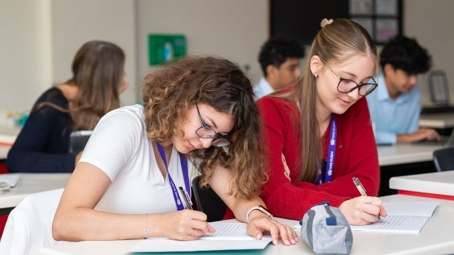 Students writing at desks in a classroom, representing active learning and the process of developing deeper understanding.