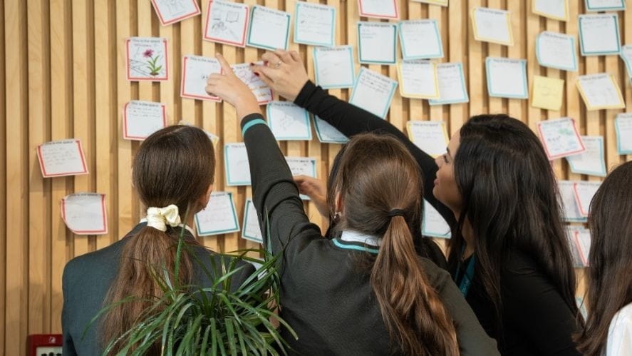 Students collaborating in an activity at NAS Dubai international school Students placing notes on a wall display during a collaborative learning activity at NAS Dubai international school