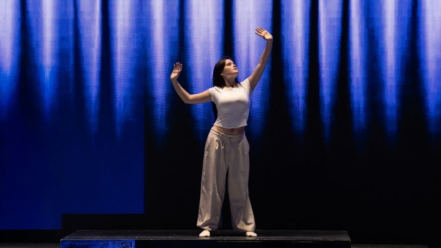 Student presenting IB solo performance on stage, captured mid-expression with dramatic lighting.