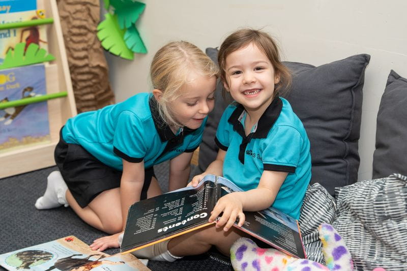Two NAS Dubai students enjoying a quiet moment of reading together in a cosy library, surrounded by books and natural light, highlighting a love of learning and reading for pleasure.