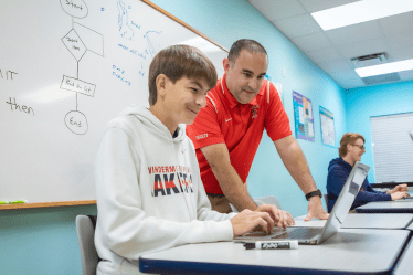 teacher-helping-student-at-laptop-in-computer-science-class