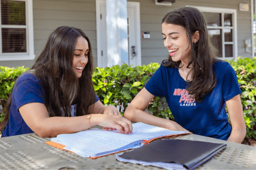 two-female-high-school-students-working-on-homework-in-courtyard